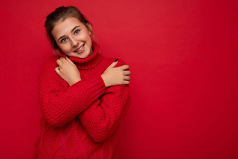 有吸引力的可爱的微笑年轻的女人穿温暖的红色的毛衣孤立的红色的背景墙保持手胸部相机