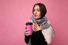 照片拍摄美丽的心烦意乱年轻的浅黑肤色的女人女人穿黑色的毛衣温暖的围巾孤立的粉红色的背景持有纸咖啡杯模型喝一边生病的
