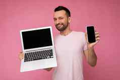 英俊的褐色男人。持有移动PC电脑移动电话相机t恤孤立的粉红色的背景