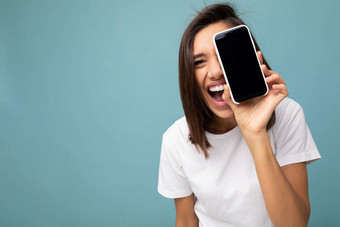 特写镜头照片漂亮的积极的年轻的浅黑肤色的女人女人好穿白色t恤站孤立的蓝色的背景复制空间持有智能手机显示电话手空屏幕屏幕断路相机