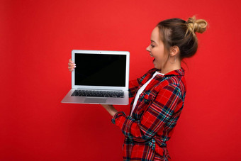 一边配置文件照片美丽的惊讶年轻的女人持有移动PC穿红色的衬衫<strong>监控</strong>显示孤立的红色的背景