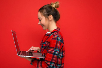 特写镜头一边配置文件照片微笑年轻的女人持有上网本显示监控打字键盘穿红色的衬衫孤立的红色的墙背景