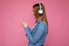 side-ptofile特写镜头照片美丽的年轻的女人穿时尚的休闲装孤立的色彩斑斓的背景墙穿白色无线耳机听音乐移动电话消息传递短信智能手机显示