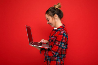 一边配置<strong>文件</strong>照片漂亮的年轻女子持有上网本屏幕打字<strong>键盘</strong>穿红色的衬衫孤立的红色的墙背景