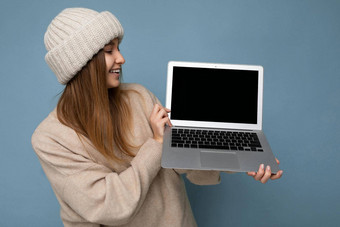 照片拍摄美丽的迷人的迷人的漂亮的微笑快乐年轻的黑暗金发碧眼的女人冬天温暖的针织米色他持有电脑移动PC上网本空免费的复制空间监控键盘穿米色冬天毛衣孤立的光蓝色的墙背景工作室