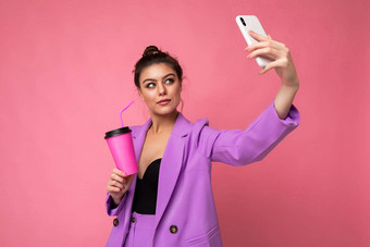 有吸引力的年轻的褐色<strong>女人</strong>时尚紫色的西装粉红色的背景工作室持有受欢迎的电话采取自<strong>拍照片</strong>喝稻草饮料