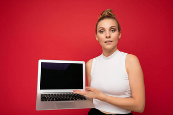 <strong>照片</strong>美丽的金发碧眼的年轻的女人<strong>聚集</strong>头发相机持有电脑移动PC空监控屏幕模拟复制空间显示上网本穿白色t恤孤立的红色的墙背景
