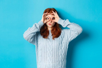 有趣的红色头发的人女模型毛衣盯着相机手指眼镜表达感兴趣惊讶的是站蓝色的背景