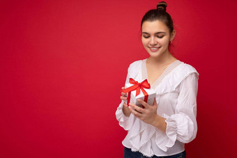 拍摄迷人的快乐微笑年轻的浅黑肤色的女人女人孤立的红色的背景墙穿白色上衣持有白色礼物盒子红色的丝带
