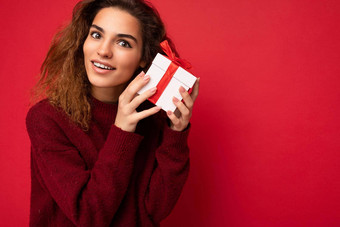特写镜头照片有吸引力的积极的微笑年轻的浅黑肤色的女人卷曲的女人孤立的红色的背景墙穿红色的毛衣持有礼物盒子相机做梦