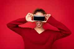照片肖像快乐有趣的年轻的女人穿黑暗红色的毛衣孤立的红色的背景持有智能手机显示移动电话屏幕空空间模型有趣的