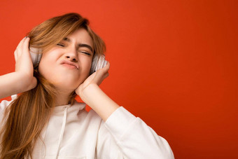 肖像照片拍摄有吸引力的情感积极的年轻的金发女郎女人穿白色连帽衫孤立的色彩鲜艳的背景穿白色无线<strong>蓝牙耳机</strong>听音乐享受有趣的