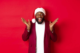 圣诞节聚会，派对假期概念惊讶快乐非洲美国男人。圣诞老人他喜乐相机站红色的背景