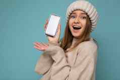 特写镜头照片惊讶美丽的积极的好年轻的女人穿时尚的米色毛衣米色针织冬天他平衡孤立的蓝色的背景空空间持有手显示移动电话空屏幕模型相机