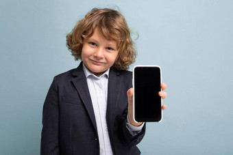 特写镜头照片英俊的积极的男孩卷曲的头发穿西装持有电话孤立的蓝色的背景相机显示智能手机空显示屏幕