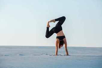 年轻的女人练习反演平衡瑜伽构成<strong>倒立</strong>沙子
