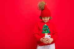 年轻的男人。智能手机手背景红色的墙针织他毛衣圣诞节树