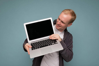 特写镜头肖像英俊的金发女郎男人。持有电脑移动PC上网本键盘穿休闲衣服孤立的蓝色的背景