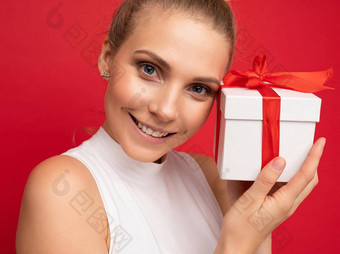 肖像照片拍摄有吸引力的快乐微笑年轻的金发女郎女人孤立的<strong>红色</strong>的<strong>背景墙</strong>穿白色前持有礼物盒子相机