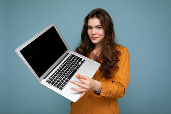 <strong>照片</strong>美丽的快乐年轻的女人持有电脑移动PC相机穿黄色的夹克孤立的蓝色的<strong>墙背景</strong>
