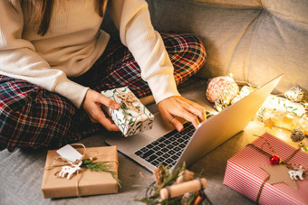 关闭女人手礼物打字移动PC在线购物圣诞节假期裁剪女坐沙发上自然生态礼物装饰快乐圣诞节包装概念