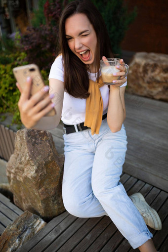 免费的年轻的女人喝咖啡聊天智能手机坐着板凳上夏天公园
