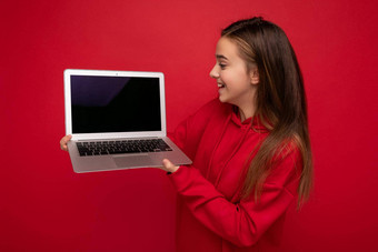 一边配置<strong>文件</strong>照片美丽的快乐女孩长头发穿红色的连帽衫持有电脑移动PC上网本<strong>键盘</strong>屏幕监控孤立的红色的墙
