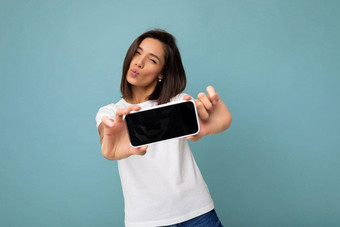 照片漂亮的积极的年轻的浅黑肤色的女人女人好穿白色t恤站孤立的蓝色的背景复制空间持有智能<strong>手机</strong>显示电话手空屏幕屏幕断路相机