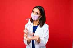 年轻的女医生白色外套保护面具把洗手液手年轻的漂亮的女人医疗统一的把防腐剂手卫生概念