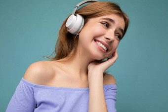 特写镜头照片漂亮的快乐微笑年轻的金发女郎女人穿蓝色的作物前孤立的蓝色的背景墙穿白色无线蓝牙耳机听很酷的音乐享受一边