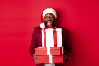 圣诞节一年购物概念快乐黑色的男人。圣诞老人他夹克持有圣诞节礼物带礼物微笑站红色的背景