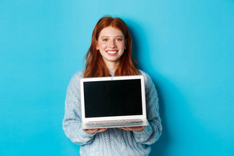 年轻的微笑女人红色的头发雀斑显示电脑屏幕持有移动PC演示在线促销站蓝色的背景