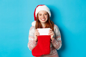 冬天假期概念快乐的女孩接收礼物圣诞节长袜穿圣诞老人他微笑快乐站蓝色的背景