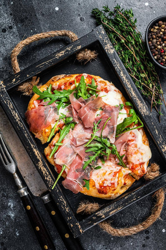 意大利披萨火腿帕尔马他芝麻菜沙拉奶酪乡村木托盘黑色的背景前视图