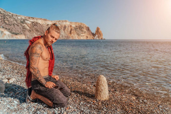 成熟的纹身男人。坐着海滩岩石祈祷准备好了战斗海<strong>背景</strong>肖像英俊的肌肉发达的古老的战士<strong>武术</strong>艺术概念