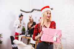 肖像年轻的女人粉红色的礼品盒首页前景美丽的金发女郎圣诞老人他红色的衬衫笼子里黑色的牛仔裤