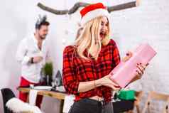 肖像年轻的女人粉红色的礼品盒首页前景美丽的金发女郎圣诞老人他红色的衬衫笼子里黑色的牛仔裤