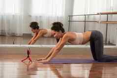 健身女人练习瑜伽看在线会议教练智能手机女运动员健身培训远程会议学习瑜伽提出了体式普拉提