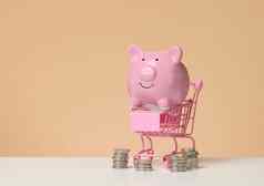 金属微型购物车粉红色的小猪银行白色表格棕色（的）背景概念储蓄预算折扣