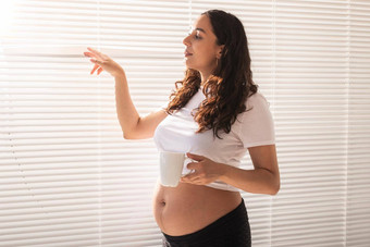 好奇的怀孕了女人喝茶百叶窗窗口概念快乐好新闻等待婴儿