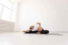 年轻的灵活的怀孕了女人体操地毯地板上白色背景概念准备身体容易分娩复制空间