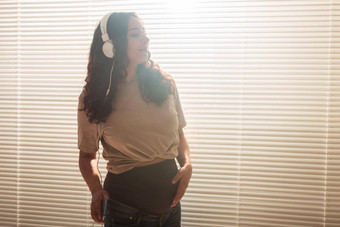 卷发浅黑肤色的女人安抚了怀孕了女人听愉快的经典音乐智能手机耳机概念舒缓的情绪会议婴儿Copyspace