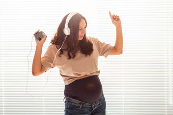 卷发浅黑肤色的女人安抚了怀孕了女人听愉快的经典音乐智能手机耳机概念舒缓的情绪会议婴儿