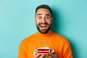 特写镜头快乐成人男人。庆祝生日持有bday蛋糕蜡烛使站绿松石背景