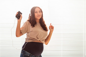 卷发浅黑肤色的女人安抚了怀孕了女人听愉快的经典音乐智能手机耳机概念<strong>舒缓</strong>的情绪会议婴儿Copyspace