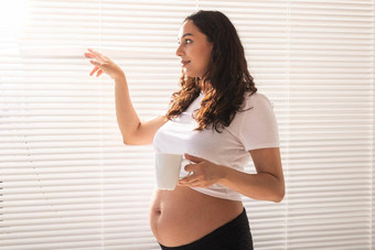 好奇的年轻的美丽的怀孕了女人喝茶百叶窗窗口概念快乐好新闻等待婴儿