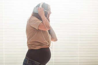 卷发浅黑肤色的女人安抚了怀孕了女人听愉快的<strong>经典音乐</strong>智能手机耳机概念舒缓的情绪会议婴儿Copyspace