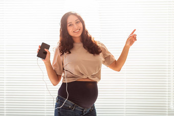 卷发浅黑肤色的女人安抚了怀孕了女人听愉快的经典音乐智能手机耳机概念舒缓的情绪会议婴儿