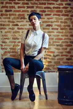 美丽的年轻的女人模型时尚短发型相机坐着椅子砖墙背景