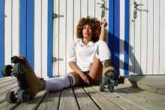 年轻的黑色的女人辊溜冰鞋坐着海滩小屋